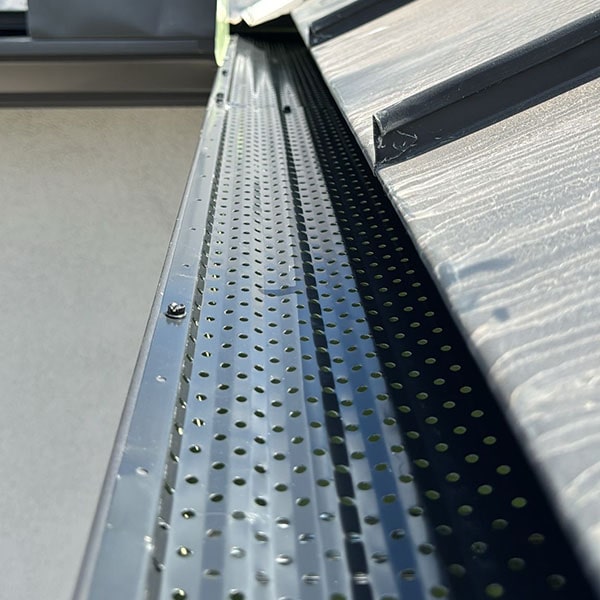 Close-up of a perforated metal sheet by a window sill, illuminated by sunlight in San Antonio, TX.