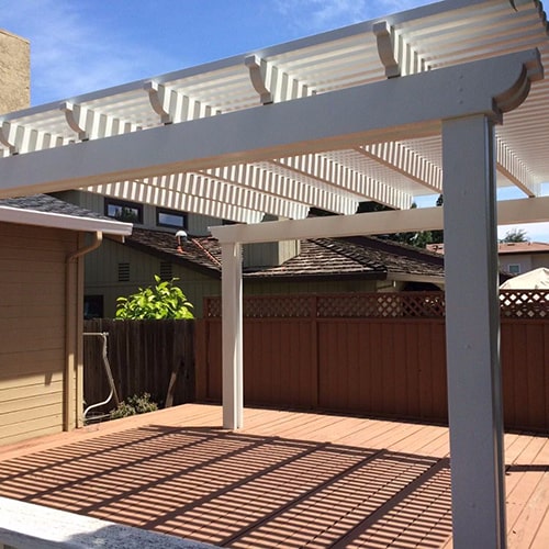 White pergola casting striped shadows on a wooden deck, with a clear sky above.