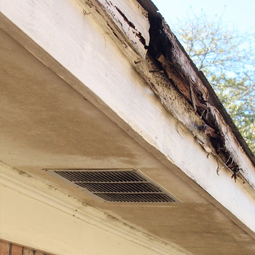 Damaged roof eave with peeling paint and exposed wood under clear sky River City Gutters in Houston, TX.