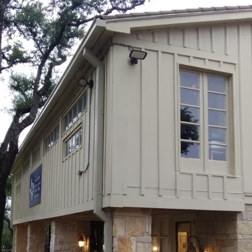 Corner of a beige building with large windows and a sign on wood paneling, surrounded by trees River City Gutters in Houston, TX.