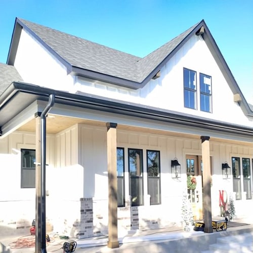 White two-story house with a gabled roof, porch columns, and clear blue sky River City Gutters in Houston, TX.